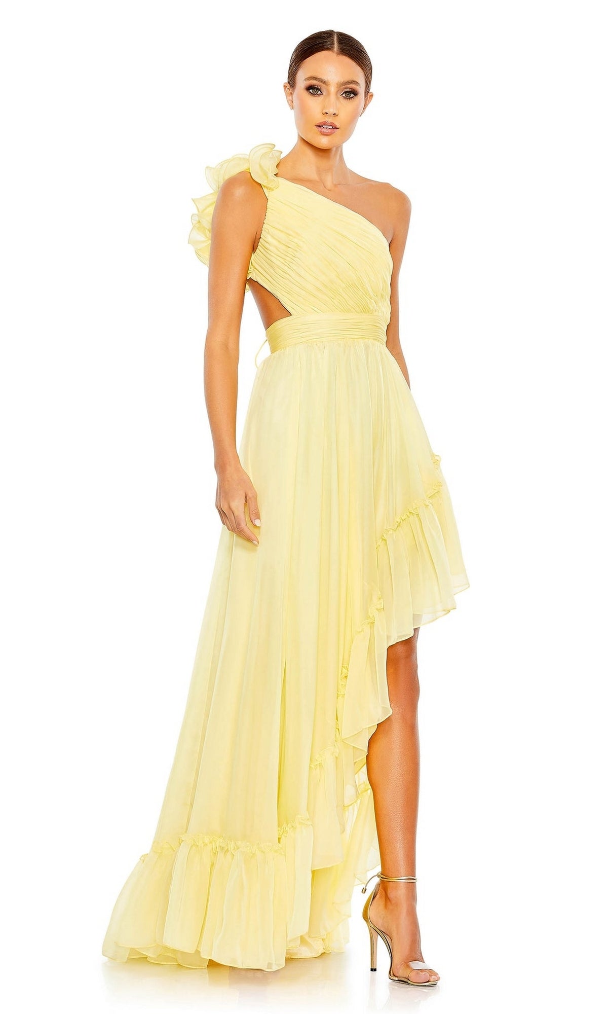 A woman wears the Long Formal Dress 67989 by Mac Duggal, featuring light yellow fabric, a one-shoulder design with ruffled details, and an asymmetrical hem, paired with strappy high heels against a plain background.